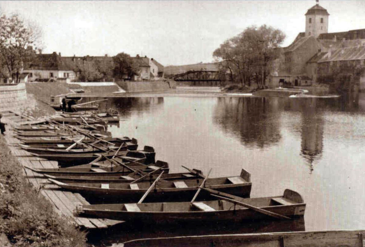 Původní plovárna na levém břehu řeky Otavy v první polovině 20. století – půjčovna loděk pana Bechyňského se siluetou hradu v pozadí