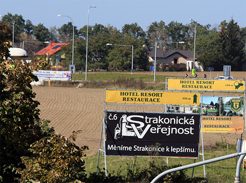 Pozemek podnikatele Radima Žahoura p.č. 269/2 v k.ú. Strakonice s reklamou na jeho restauraci a hotel Lovecká bašta a na Strakonickou Veřejnost v popředí – za nimi vzadu vlevo reklama Volby pro město na okružní křižovatce na pozemku firmy GARANTSTAV ST, s.r.o. podnikatele Radima Žahoura p.č. 270/5 v k.ú. Strakonice (prostorově zkresleno teleobjektivem).